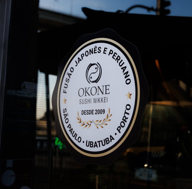 Selo no vidro do Okone Sushi Nikkei com os dizeres Fusão Japonês e Peruano, citando São Paulo, Ubatuba e Porto desde 2009