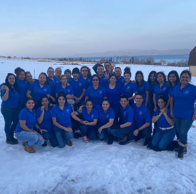 A large group of employees in blue polo shirts posing together in a snowy field with a lake view.