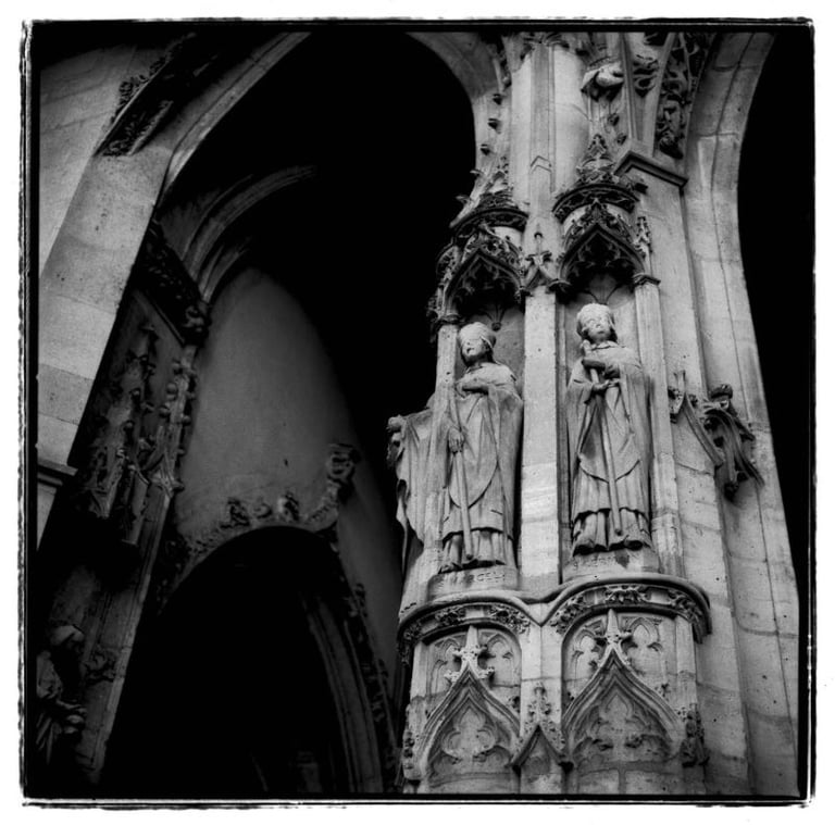 A picture of an architecture in Paris, an entrance to the old church. A column with two sculptures. Creator: Slawek Dejneka