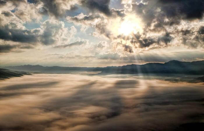 Fog-covered mountains with sunbeams piercing through dramatic clouds.
