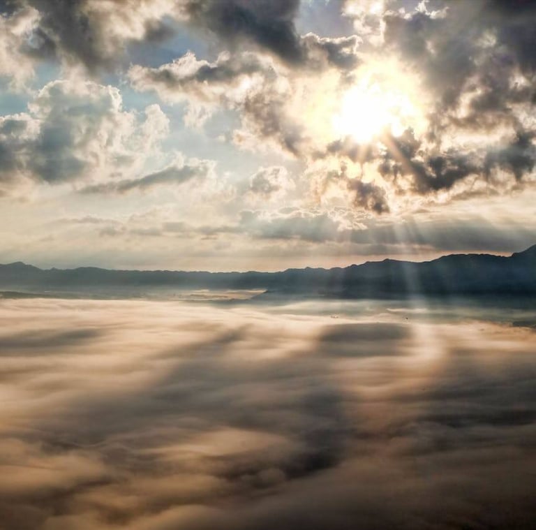a view of a mountain range with clouds and sun shining through the clouds