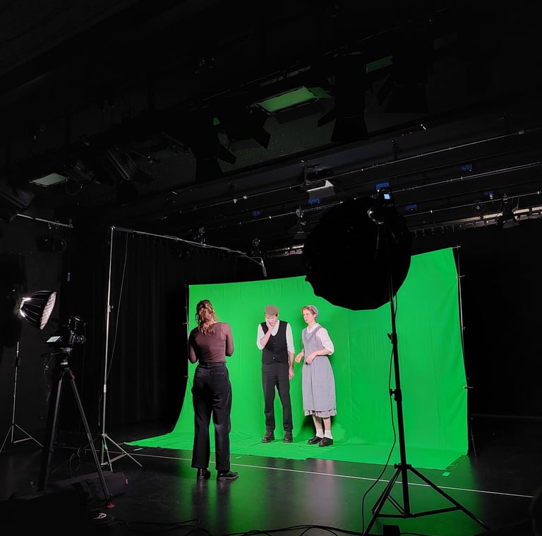 Zwei Schauspieler:innen in einem Greenscreen-Set, während die Regisseurin ihnen etwas erklärt.