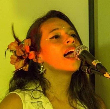 Cantante femenina con una flor en el cabello, interpretando en vivo frente a un micrófono 