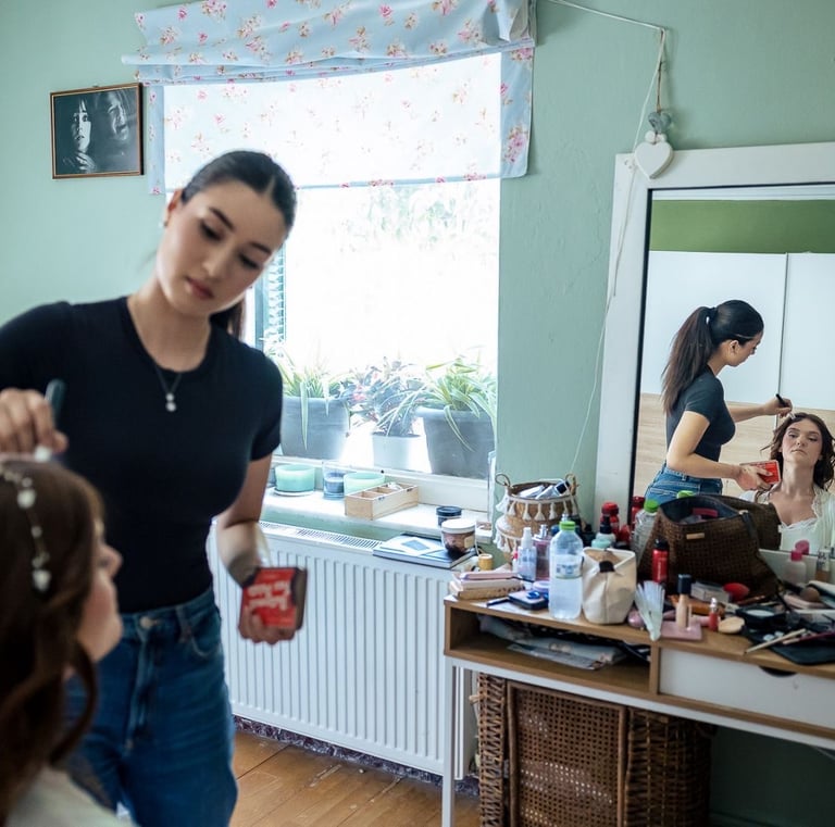 Bride sitting at vanity while makeup artist adds finishing touches — elegant bridal photo prep