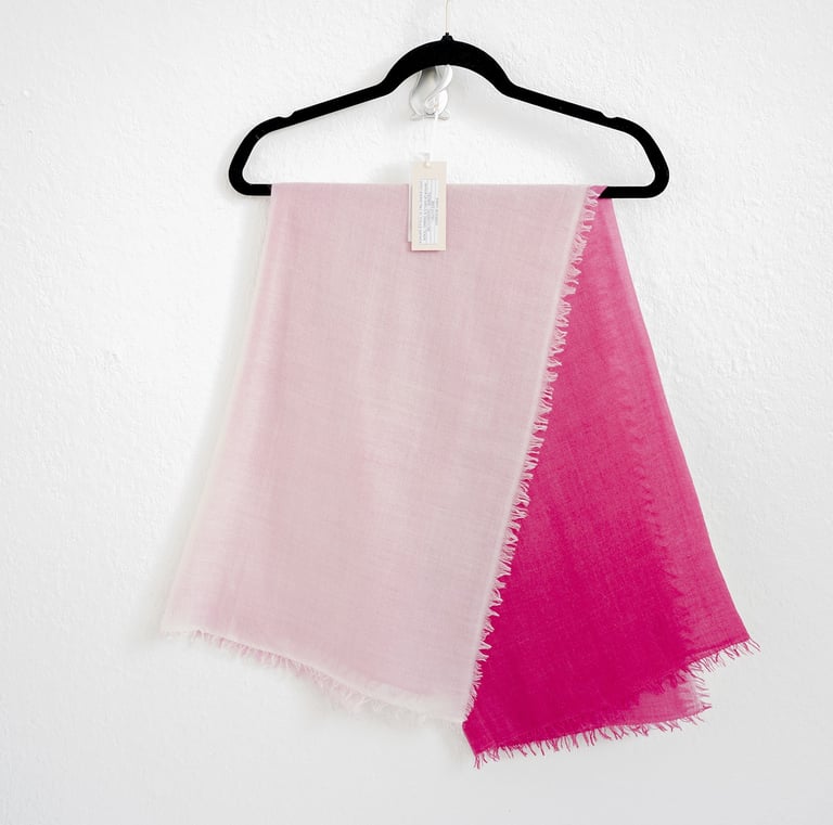 Two-tone pashmina scarf in soft pink and vibrant fuchsia, hanging neatly on a black hanger display.