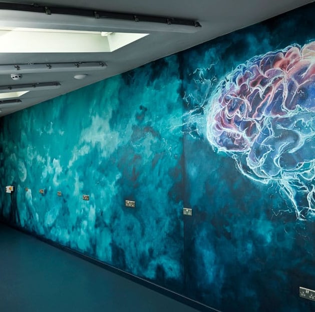 Dark teal mural in modern R&D interior, showing stormy clouds and a stylised brain with pink highlighted areas.