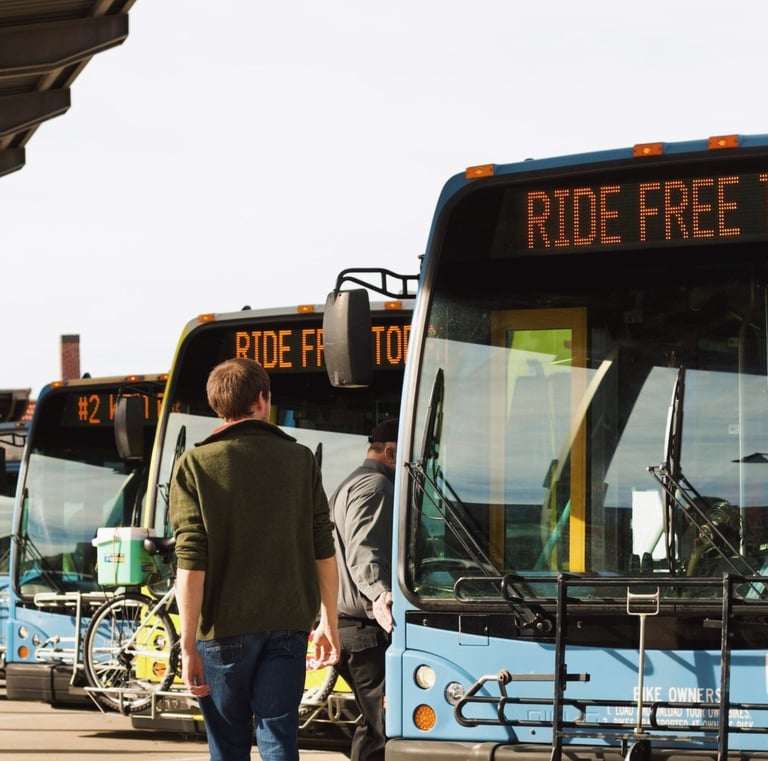 Man walking in front of a line of buses with the bus route sign reading "Ride Free Today"