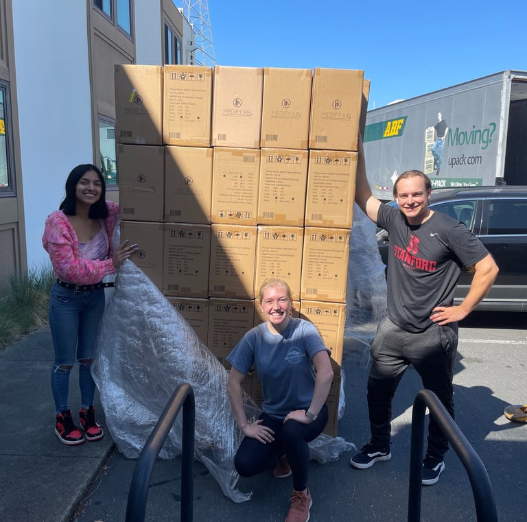 Three people with a large pallet of air purifiers in boxes