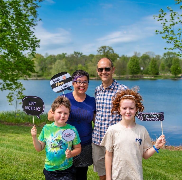 Two parents and two children posing in front of a lake holding sign props