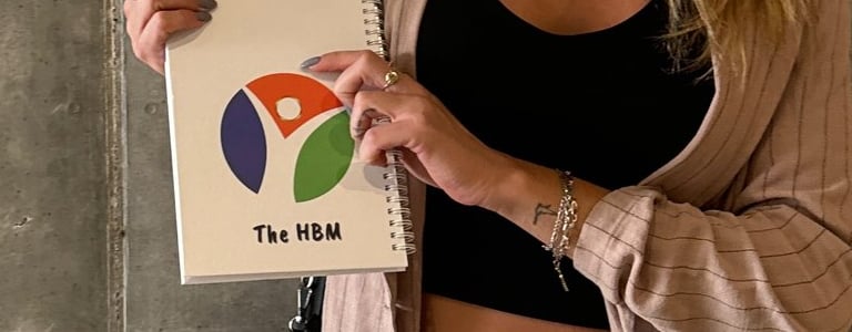 משתתפת בסדנת 'ארנק כוחות העל שלי' מחזיקה ארנק כוחות על וחוברת הסדנה, עם חיוך וביטחון.