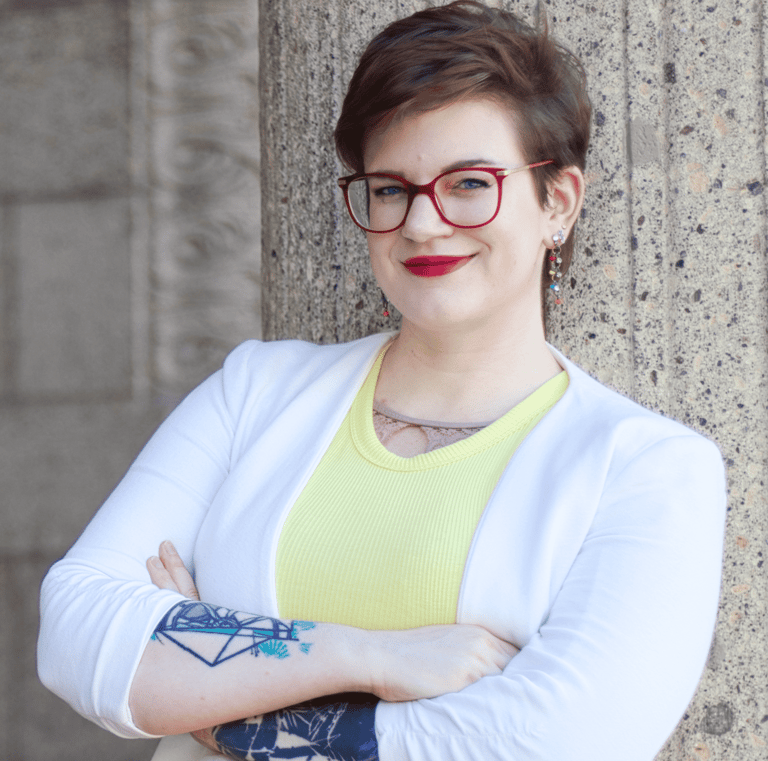 a photo of Swana Schuchmann with short hair, a white blazer and glasses, smiling
