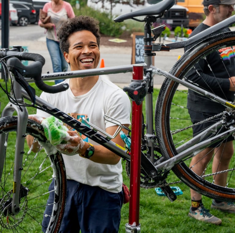 A young man smiling and washing a bike held high on a stand