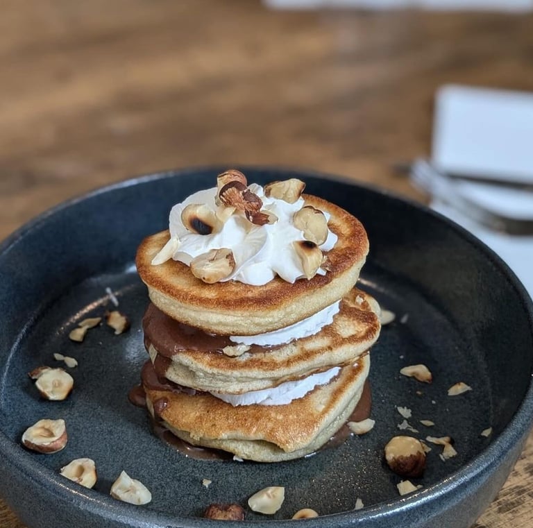 une assiette sur une table en bois avec une tour de pancakes et chantilly