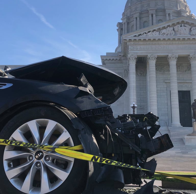 The front of a car that has been in a wreck, with the Missouri capital building in the background