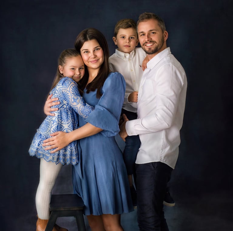 a family of four posing in a studio for a family portrait, all wearing blue and white