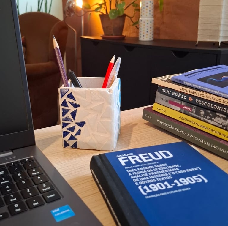 Mesa de trabalho com livros de autoras como Ana Suy, Gayle Rubin e Geni Núñez, ao lado do notebook u