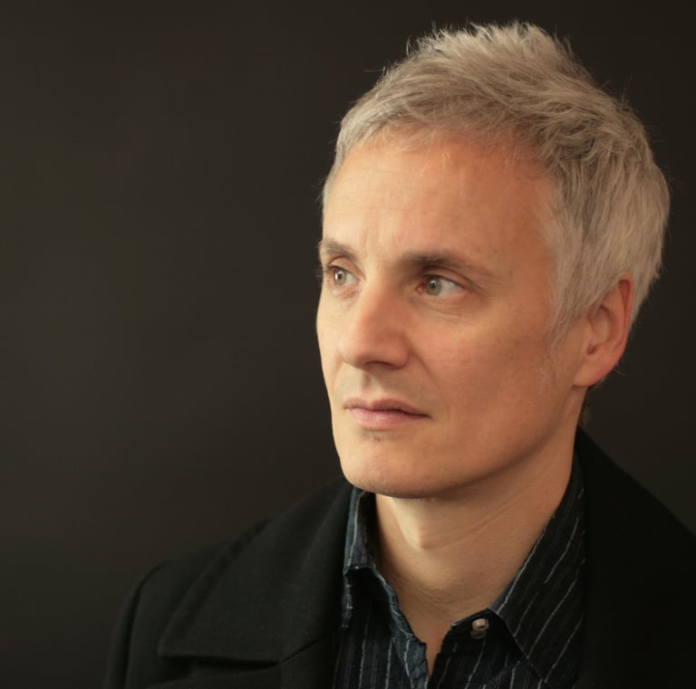Professional portrait of a man with short grey hair and green eyes looking aside against a dark background.