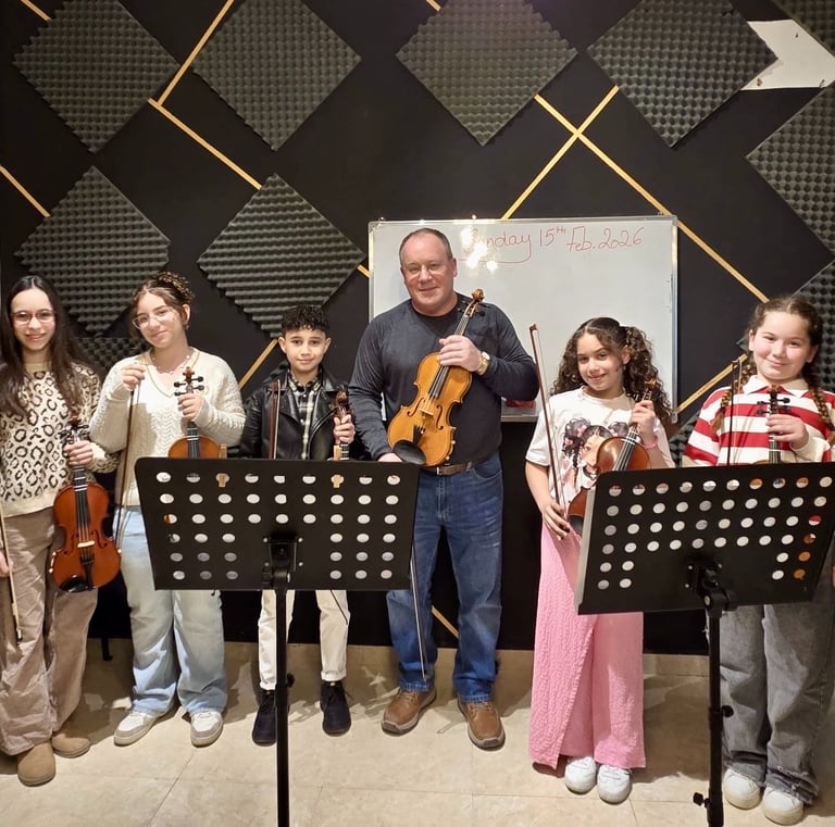 A smiling music teacher and his diverse group of violin students pose with their instruments in a sound-proofed studio.