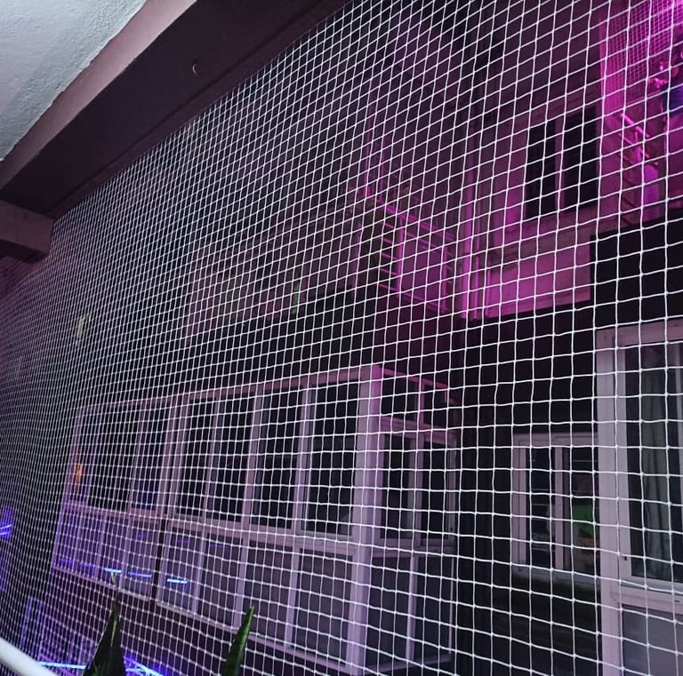 Wide shot showing a high-rise balcony fully covered with fine mesh netting to keep pigeons out.