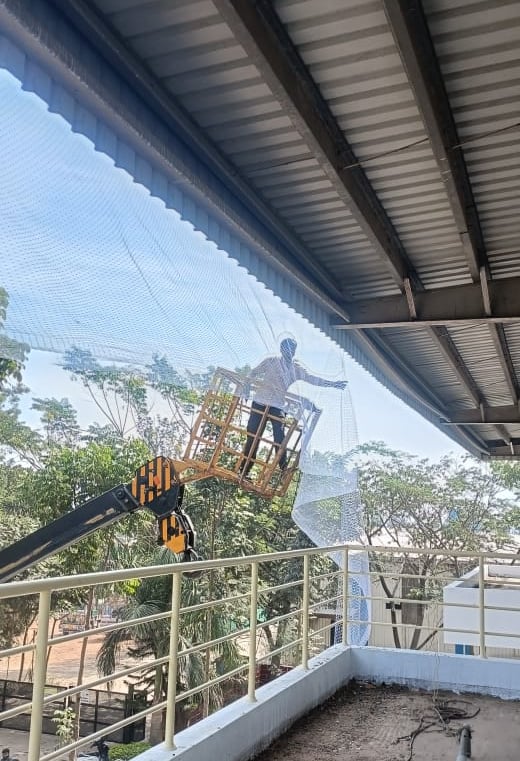 Technician carefully fixing pigeon netting along the warehouse roof edge.