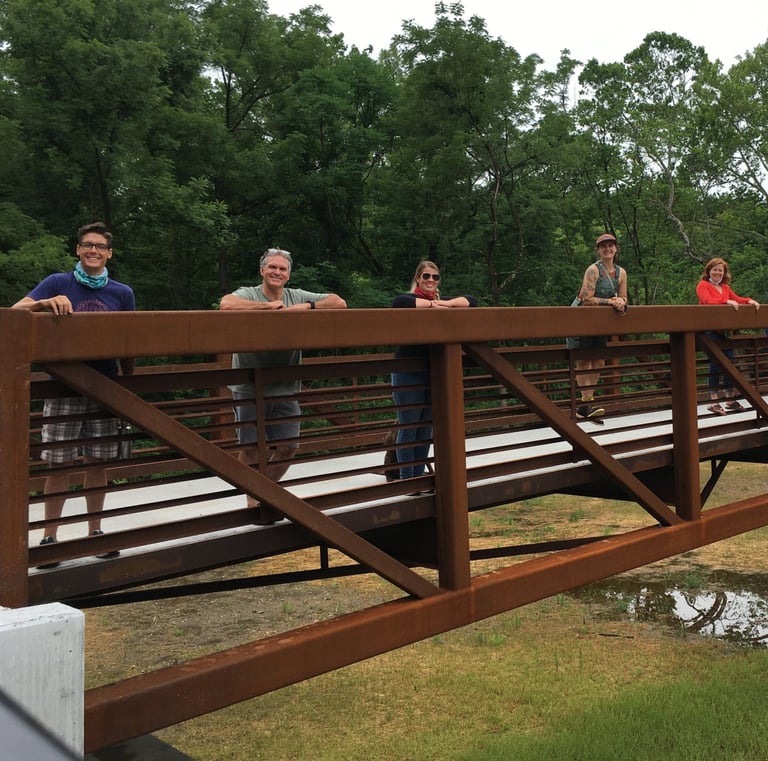 Photo of people standing in a line on a trail bridge smiling at the camera