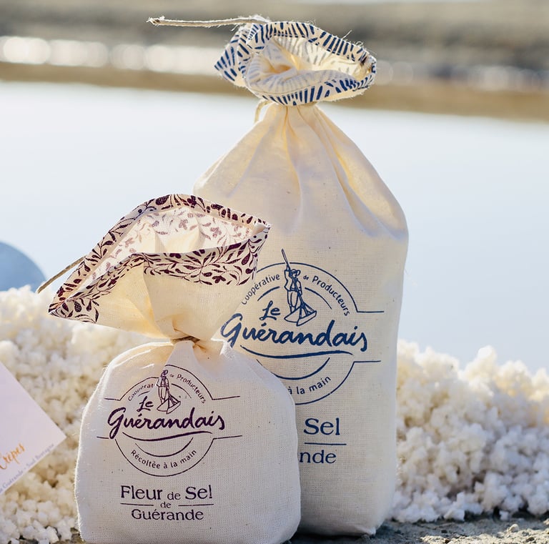 2 sachets en tissus de sel de Guérande posés à côté d'un tas de gros sel