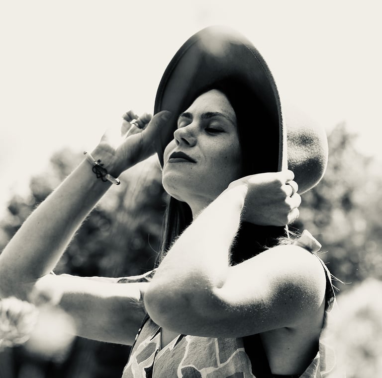 Photo en noir et blanc d'une jeune femme qui lève la tête et qui retient avec ses mains son chapeau
