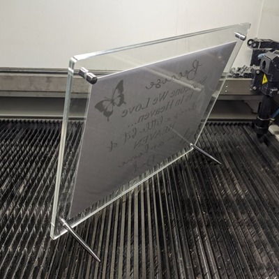 Acrylic standee frame displaying engraved text on a metal surface