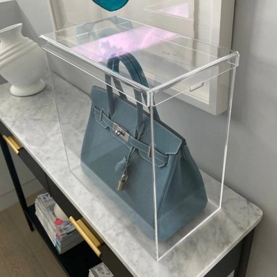 Clear acrylic display case showcasing a blue handbag on a marble table.