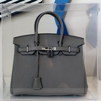 Clear acrylic display case with a grey handbag inside.