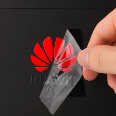 Clear UV DTF transfer sticker being peeled off a red Huawei logo.