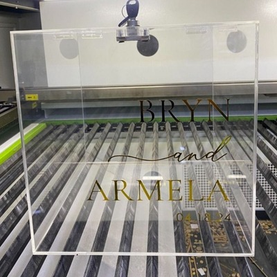 Clear acrylic wedding box with 'Bryn and Armela 04.08.24' in gold and black lettering.