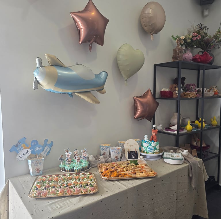 Baby shower catering table with an airplane balloon, blue cupcakes, and finger food platters.