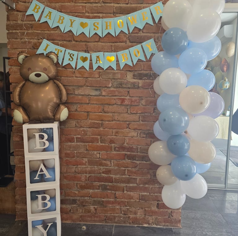 Baby shower decorations for a boy featuring a teddy bear balloon and blue balloon arch.