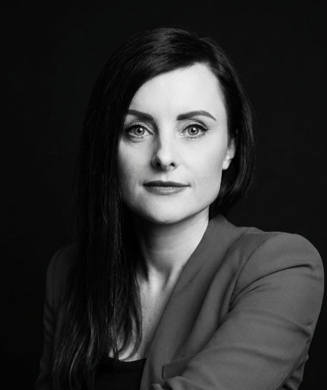 Professional black and white corporate headshot of a brunette woman against a dark background.