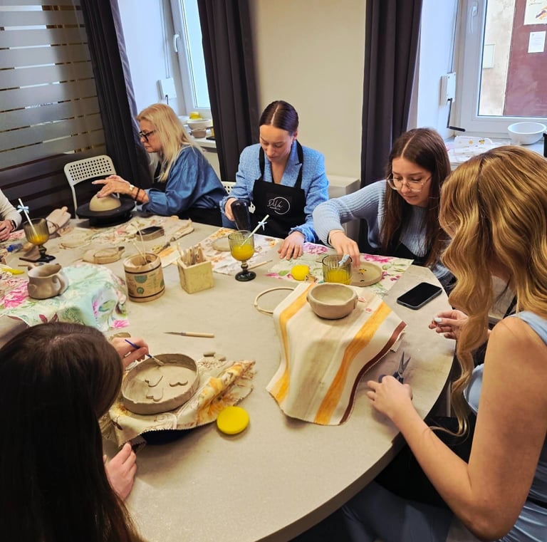 People participating in a handmade pottery workshop, sculpting and painting clay bowls at a studio table.