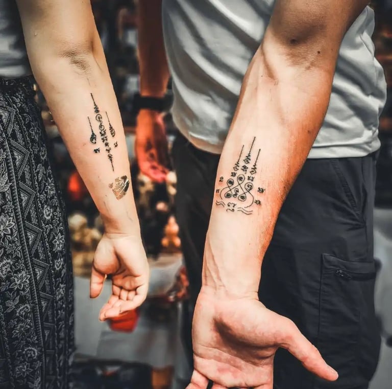 a couple holding hands with matching traditional thai tattoos sak yant on their arms