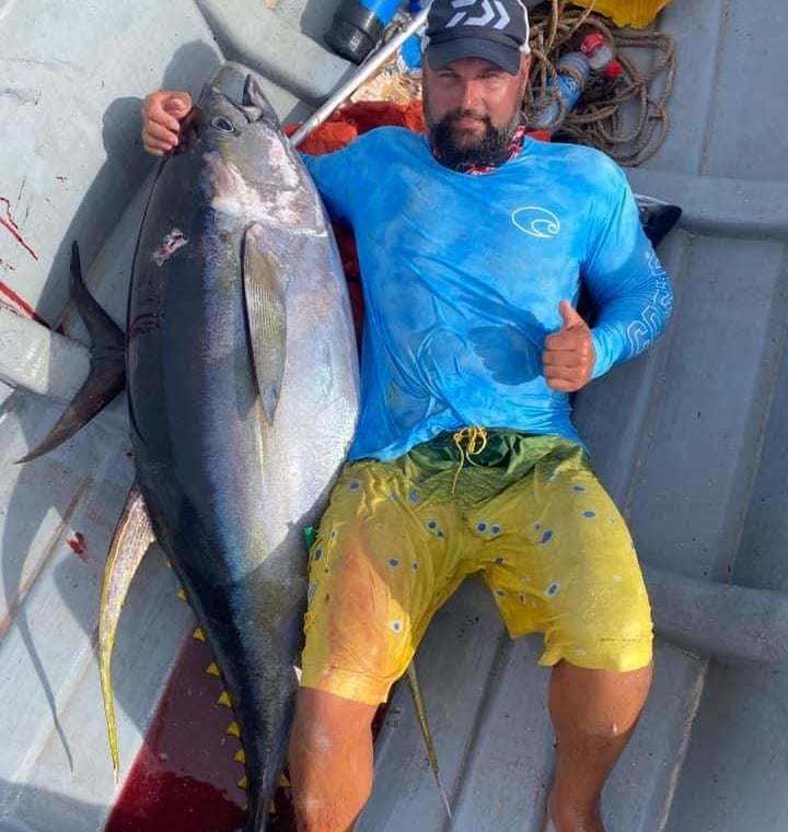  A man in a blue shirt is holding a huge yellowfin tuna on a Zanzibar fishing charter
