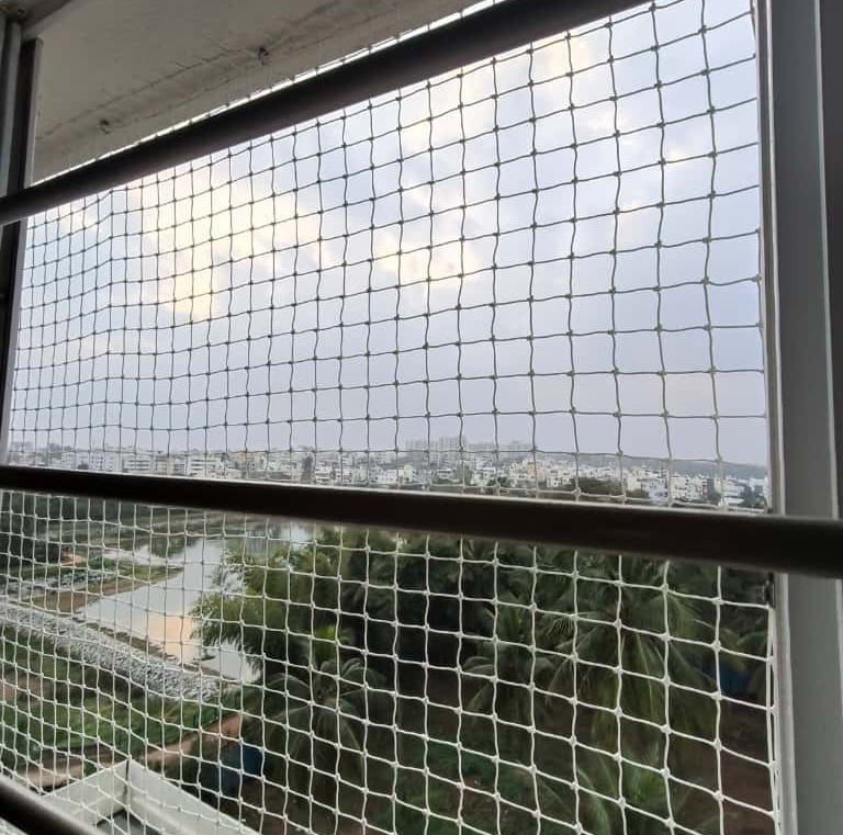 Technician carefully fixing pigeon net on a window frame in a high-rise apartment.