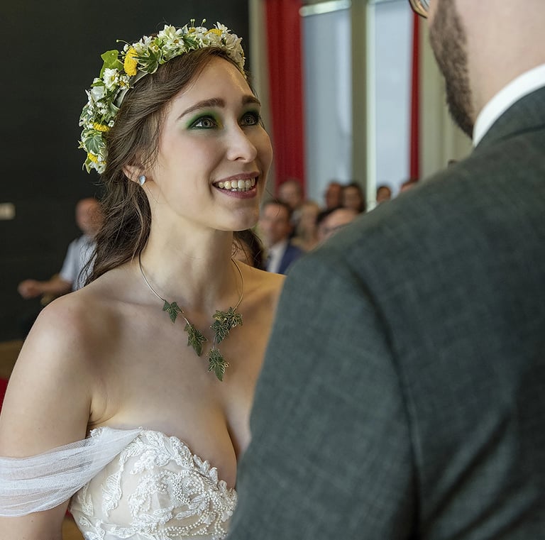 Ein Nahaufnahme-Foto einer lächelnden Braut, die nach oben zu ihrem Bräutigam blickt, dessen Rücken teilweise im Vordergrund 