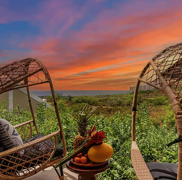 Hanging chairs overlooking a lush Hawaiian landscape during a colorful sunset at a wellness retreat,