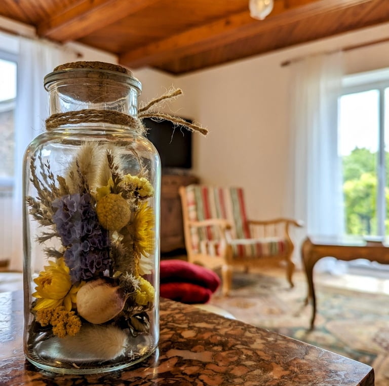 un pot de fleurs séchées dans un bocal et en arrière plan le salon