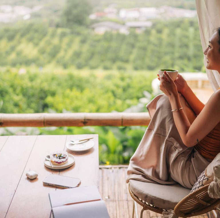 A woman drinks matcha tea on a scenic balcony overlooking a lush green valley landscape.