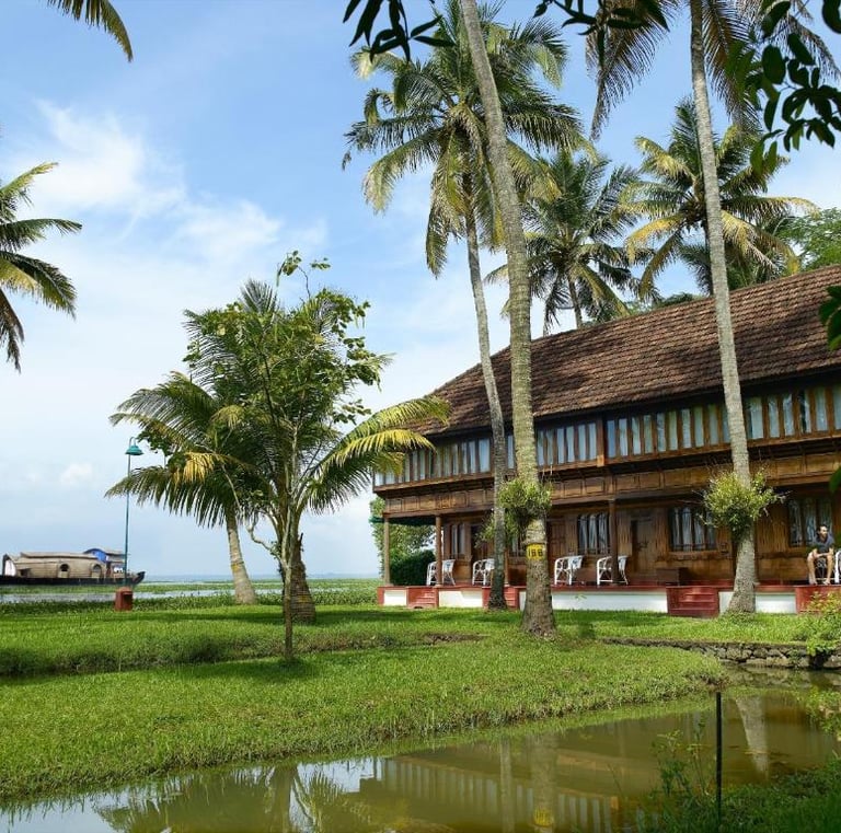 Traditional Kerala house surrounded by palm trees and lush greenery, overlooking tranquil backwaters.