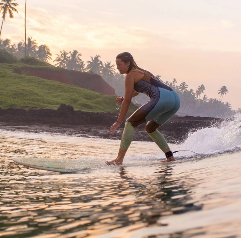 Girl surfing on a wave in Varkala, Kerala, with palm trees and cliffs in the background during sunrise.