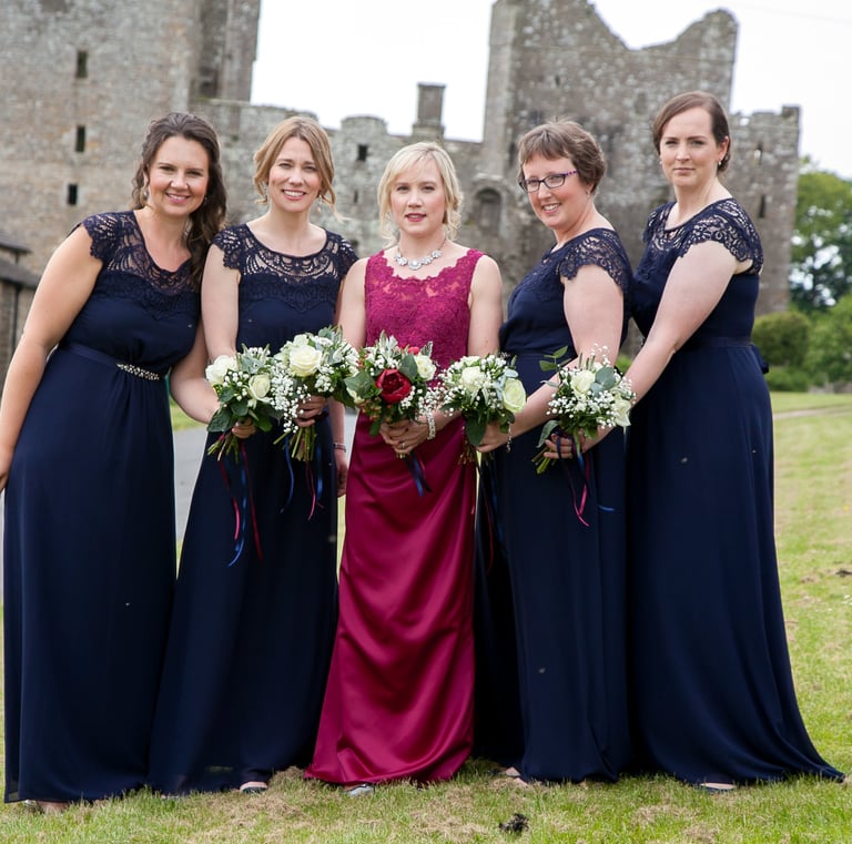 Bride with bridemaids, all stood in a row with boquets all held together. Castle in the beeeeeee
