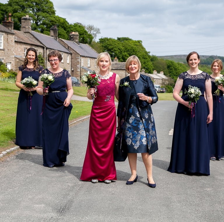 Bride with her bridesmaids. Mother is standing next to bride. Whole group are in a dart formation.
