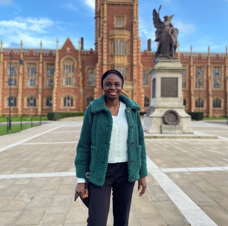 Lady in green cardigan, coat and black trousers posing in front of Queen's University Belfast