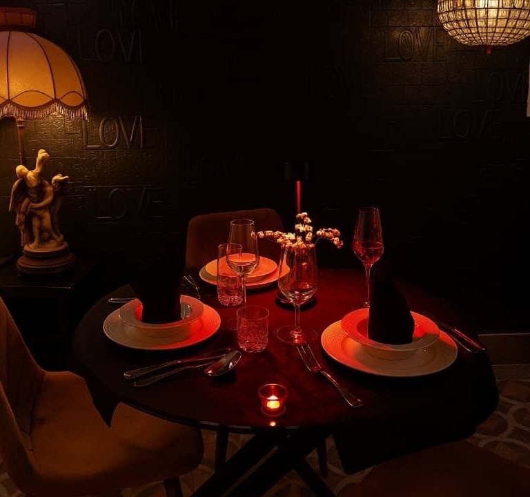 Romantic candlelit dinner table for two with wine glasses and elegant lamp lighting.