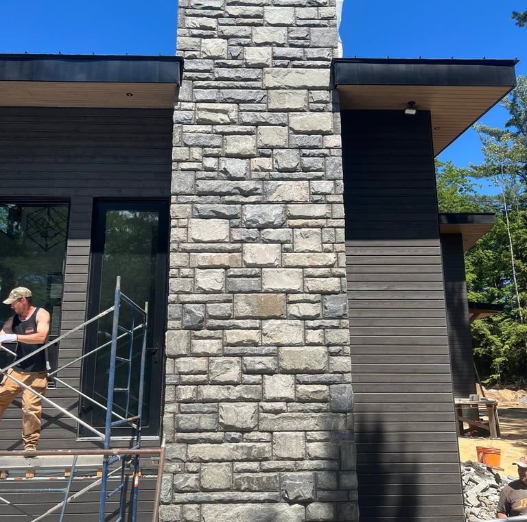 A modern home exterior featuring a natural stone veneer fireplace chimney and dark grey wood siding.